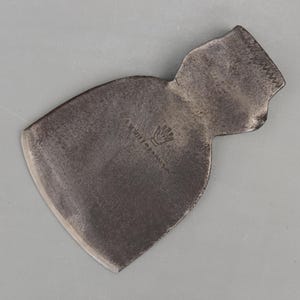 May include: A vintage, weathered metal axe head with a curved blade and a textured handle area. The axe head has a dark, aged appearance, with visible wear and tear. The manufacturer's mark is visible on the surface.