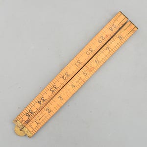 May include: A vintage wooden folding ruler, featuring inch measurements from 1 to 35. The ruler is light brown with black markings and numbers. The ruler is made of wood and has brass hinges. The ruler is a measuring tool.