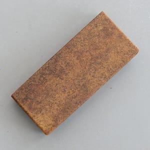 Puede incluir: Una piedra de afilar rectangular marrón con una superficie rugosa y texturizada.