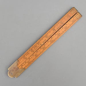 May include: A folding wooden ruler with brass hinges and metal end caps. The light brown wood features black printed imperial measurements and markings. Text on the ruler includes J. RABONE & SONS, BIRMINGHAM, ENGLAND, and No. 1178.