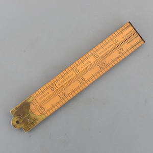 May include: A vintage wooden folding ruler with brass hinges. The ruler is marked with numbers and lines for measurement in inches. The text "E. Preston & Sons" and "DIRUS ENG" are visible. The ruler is a light brown colour.