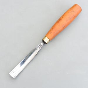 Op de afbeelding: Een houtsnijbeitel met een gepolijst stalen lemmet en een lichtbruine houten handgreep. De handgreep is cilindrisch en loopt iets taps toe naar het uiteinde. Het lemmet is gebogen en heeft een scherpe rand. De guts is ontworpen voor houtbewerking.