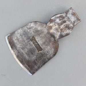May include: A vintage axe head with a weathered, metallic appearance. The axe head features a curved blade and a textured surface, with the text "STANIFORTH'S EVERQUICK" stamped on the surface. The axe head is a tool.