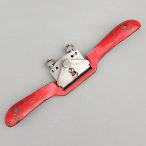 May include: A red and silver hand plane tool with a curved handle and a blade. The tool has the text "RECORD" and "A151" on the blade housing. The handle has a hole for hanging.