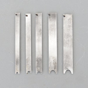May include: Six silver metal blades with different shaped edges, likely for a woodworking tool.