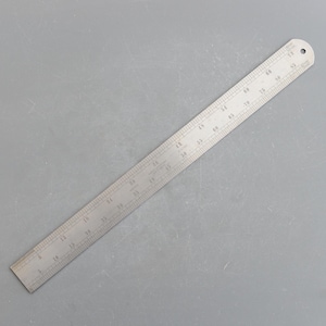 May include: A stainless steel ruler with inch and fractional markings. The ruler is approximately 24 inches long, with a hole at one end for hanging. The markings are etched into the metal, providing clear and precise measurements.