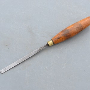 May include: A wooden handled chisel with a metal blade. The handle is brown and has a ribbed texture. The blade is silver and has a slight curve.