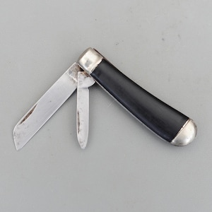 May include: A classic pocket knife featuring a black handle with silver-coloured metal ends. The knife has two open blades, one large and one small, showing signs of use. The handle is a dark, solid colour.