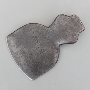 May include: A vintage, weathered metal axe head with the text "CHIP CHOP No. 1" stamped on the surface. The axe head has a curved blade and a textured, aged appearance, suggesting it's a tool for woodworking or similar tasks.