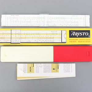 Puede incluir: Una colección de reglas de cálculo y accesorios antiguos. La imagen muestra una regla de cálculo blanca, una caja amarilla con la palabra "ARISTO", una funda blanca y roja y una hoja de instrucciones plegada. Las reglas de cálculo tienen varias escalas y marcas.