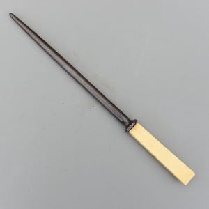 May include: A steel knife sharpening rod with a dark grey shaft and a rectangular off-white handle. The rod tapers to a point and is designed for sharpening knives. The handle is smooth and rectangular.