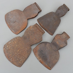 Może przedstawiać: Cztery antyczne, zardzewiałe głowice topora. Każda głowica ma ostrze w kształcie serca i prostokątny wierzch na trzonek. Metal ma zwietrzały, brązowy wygląd, sugerujący wiek i użytkowanie. Topory są ułożone na neutralnym tle.