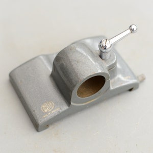 May include: A grey metal clamp with a silver handle and a round opening. The clamp has the words "Miller Walls" and "Made in England" printed on it.