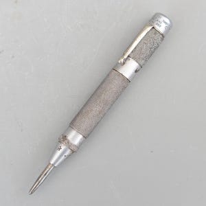 May include: A silver metal centre punch with a textured handle and a pointed tip. The handle is marked "Sheffield England No. 200".