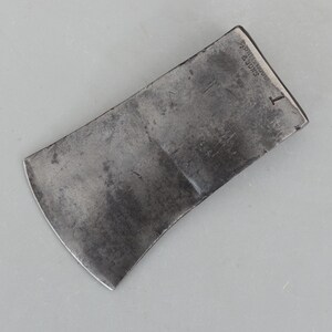 May include: A vintage axe head with a curved blade and a rectangular top. The metal has a worn, gray appearance with visible markings, including the text "CORTENOUS & SONS" and the number "1".