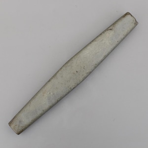 May include: A worn, rectangular metal object with a gently narrowing form. The item has a muted, silver-grey hue and seems to be constructed from a solid material, possibly steel. The surface displays signs of use and age.