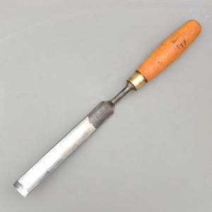 Puede incluir: Un formón para carpintería con mango de madera y hoja de metal. El mango es de color naranja claro y la hoja es plateada. El formón está diseñado para dar forma y cortar madera. El formón mide aproximadamente 23 cm de largo.