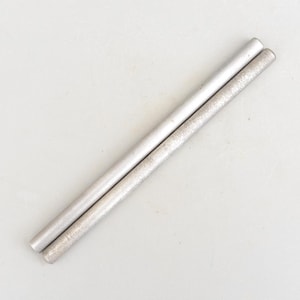 Peut inclure: Deux tiges métalliques argentées, parallèles sur un fond gris clair. L'une a une surface lisse et brillante, l'autre une apparence texturée et légèrement rugueuse. Les tiges cylindriques semblent être en métal.