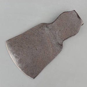 May include: A weathered, antique metal axe head with a curved blade and a textured, dark gray surface. The axe head has a wide, rectangular shape with a curved cutting edge and a slightly curved top.