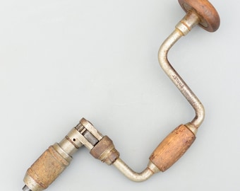 Op de afbeelding: Een vintage handboor met een houten handvat en een metalen kruk. De boor is gemaakt van metaal en heeft een zilveren afwerking. Het handvat is gemaakt van hout en heeft een bruine afwerking. De boor heeft een metalen kruk die wordt gebruikt om de boor te draaien. De boor is in goede staat en is goed onderhouden.