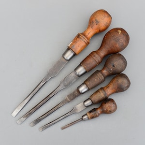 Może przedstawiać: Zestaw pięciu vintage śrubokrętów z drewnianymi uchwytami. Śrubokręty mają różne rozmiary i są w dobrym stanie.