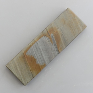 Può includere: Una pietra per affilare rettangolare con un aspetto naturale e strutturato. La pietra presenta una miscela di tonalità beige, grigie e marroni, con motivi di venature visibili. È progettata per affilare coltelli e utensili.