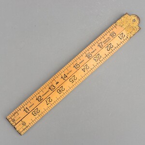 May include: A vintage wooden folding ruler with black markings and numbers. The ruler is marked with the words "England" and "Patent No. 1173229". The ruler measures up to 71 cm.
