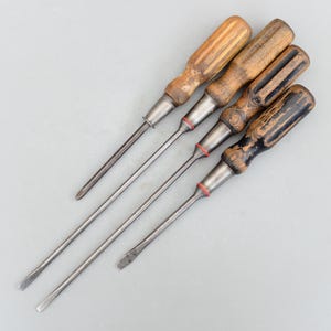 Könnte beinhalten: Vier Vintage-Schraubendreher mit Holzgriffen. Zwei haben Schlitzköpfe, einer ist ein Kreuzschlitz und einer hat ein einzigartiges geschlitztes Design. Die Griffe weisen Abnutzungserscheinungen auf, und die Metallschaft sind silberfarben. Ein klassisches Werkzeugset.