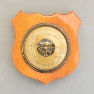 Puede incluir: Un barómetro antiguo con una cara de latón y un dial de vidrio, enmarcado en madera. El dial tiene una escala con marcas para "Muy seco", "Tiempo estable", "Mucha lluvia" y "Tormenta".