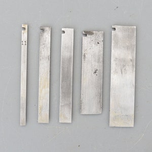 Puede incluir: Cinco cuchillas de metal con una ligera curva en la parte superior. Las cuchillas tienen todas el mismo ancho pero varían en longitud. La cuchilla más corta está etiquetada como "11".