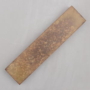 May include: A rectangular sharpening stone with a mottled, textured surface. The stone has a gradient of colors, ranging from light brown to dark brown. The stone is designed for sharpening tools.