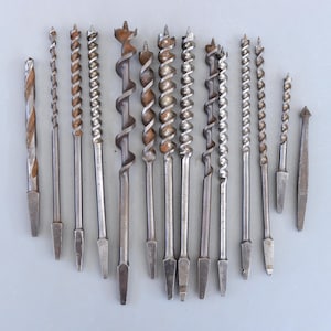 Może przedstawiać: Zestaw 14 wierteł vintage ze srebrnym wykończeniem. Wiertła są ułożone w rzędzie na szarym tle.