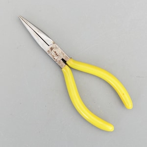May include: Needle-nose pliers with a silver metal head and bright yellow handles. The pliers are designed for precision work and feature a long, tapered nose. The handles are curved for a comfortable grip, and the tool is set against a gray background.