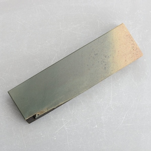 May include: A rectangular sharpening stone, approximately 20 cm long, with a grey surface and a slightly textured appearance. The stone has a gradient of colours, transitioning from grey to a tan hue. Designed for sharpening knives.