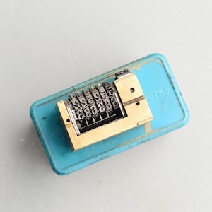 May include: A close-up of a brass number wheel with a blue plastic case. The case has the word "Werko" printed on it. The number wheel has a series of numbers visible, including 3, 4, 5, 6, 7, 8, and 9.