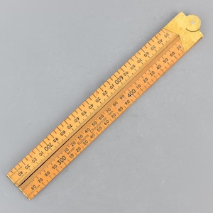 May include: A vintage wooden folding ruler, featuring measurements in increments. The ruler is light brown with black markings and numbers. The ruler is marked "Rabone Chesterman 1976".