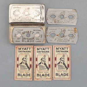 Könnte beinhalten: Eine Sammlung von Vintage Myatt Daymark Rasierklingen und -etuis. Die Metallgehäuse sind silberfarben mit Text und einer Grafik eines Mannes. Die Papierklingenverpackung ist rot und weiß mit den Worten "Blade" und "Trade Mark".