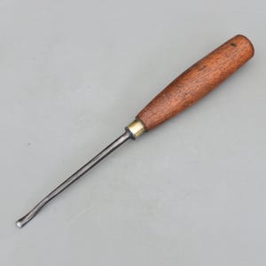 May include: A woodworking gouge with a curved blade and a wooden handle. The handle is a dark brown color, and the blade is a silver color. The gouge is designed for carving and shaping wood. The tool is approximately 8 inches long.