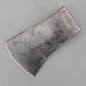 May include: A weathered metal axe head with a curved blade. The axe head has the text "-BRADES-" and "10415" stamped on the top. The metal has a worn, textured appearance.