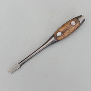 May include: A vintage flathead screwdriver with a wooden handle. The handle is a light brown color with two silver rivets. The metal shaft and head are a silver color. The tool is designed for turning slotted screws.