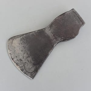 以下が含まれることがあります： 曲がった刃とフレア状の長方形の柄が付いた、風化した濃い灰色の斧頭。 金属表面には摩耗や経年劣化の兆候が見られ、テクスチャや変色も確認できます。 斧頭は木工や同様の作業向けに設計されています。