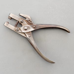 May include: A silver metal hand punch tool with a serrated handle. The tool is labelled "BLISS  MFG. CO.  PATENTED  OCT. 27, 1903".