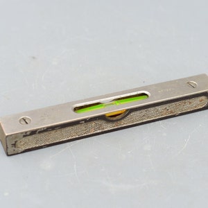 May include: A silver metal level with a green bubble level. The level has a textured surface and a small screw on each end.