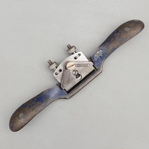 May include: A vintage hand plane with a blue handle and a silver metal blade housing. The tool has two adjustment screws and the word "RECORD" is visible on the blade housing. The handle has a hole for hanging.