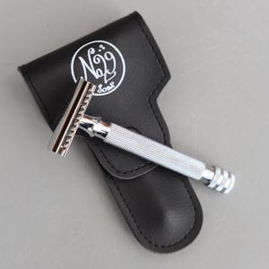 May include: A chrome safety razor with a textured handle lies on a black leather case. The case features a white circular logo with the text "No. 29 Soap". The razor is designed for shaving.