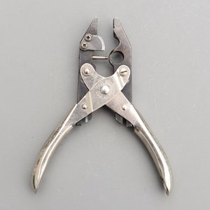 Puede incluir: Alicates plateados con mangos negros y una etiqueta "SIMPLEX". Los alicates tienen una herramienta de crimpado en un lado y un cortador de alambre en el otro.