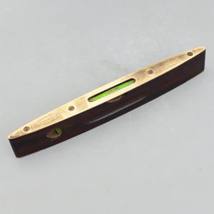 May include: A vintage level with a dark wood body and brass accents. The level has a green bubble vial and is marked with text. The tool is designed for measuring horizontal and vertical alignment.
