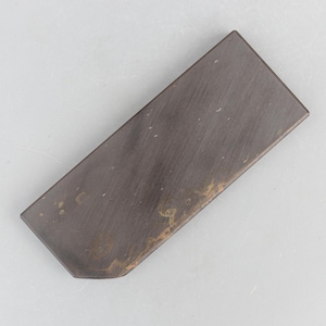 May include: A rectangular sharpening stone with a dark charcoal grey surface featuring subtle brown and tan mineral inclusions. The stone has a smooth, flat top face and a slightly angled corner on one end, displaying a natural, matte texture.