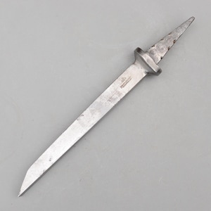 May include: A vintage, metal dagger with a long, rectangular blade and a distinctive handle. The blade tapers to a sharp point. The handle has a rectangular bolster and a textured, pointed tip. The metal has a worn, aged appearance.