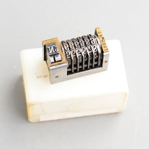 May include: A silver and gold-toned number counter with a series of rotating wheels. The counter is labelled "No. 1941".